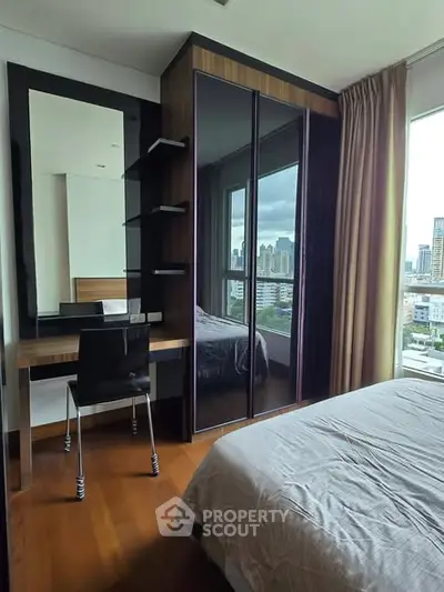 Modern bedroom with city view, featuring a sleek desk and mirrored wardrobe.