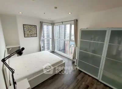 Modern bedroom with city view, featuring sleek furniture and large windows for natural light.