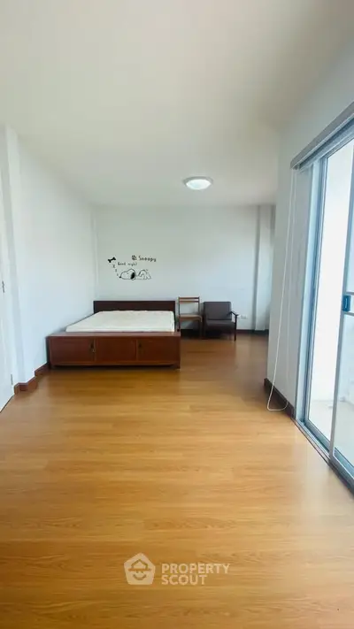Spacious bedroom with wooden flooring and sliding glass doors to balcony.