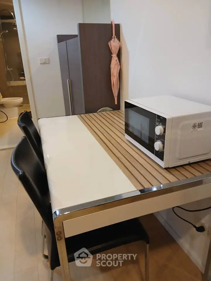 Modern kitchen with sleek table, chairs, and microwave, adjacent to a bathroom, showcasing compact urban living.
