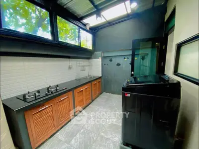 Modern kitchen with gas stove and washing machine, featuring sleek design and ample natural light.
