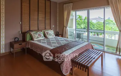 Spacious bedroom with large windows and balcony overlooking lush greenery.