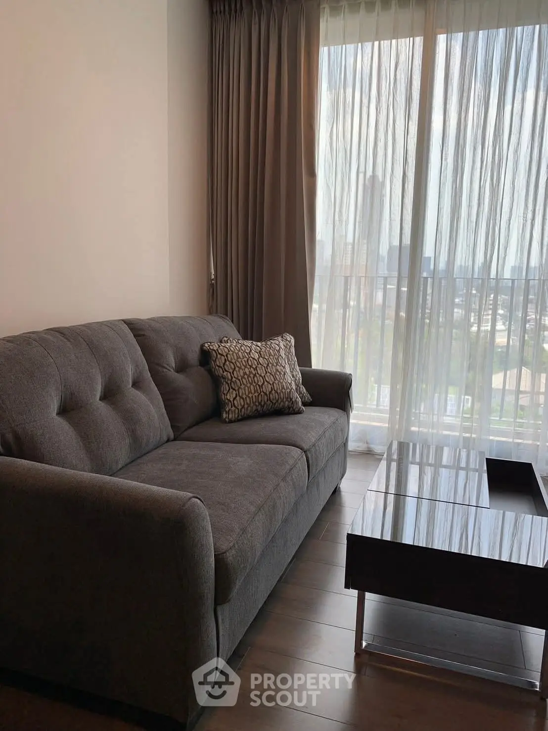 Modern living room with gray sofa and glass coffee table, featuring floor-to-ceiling window view.