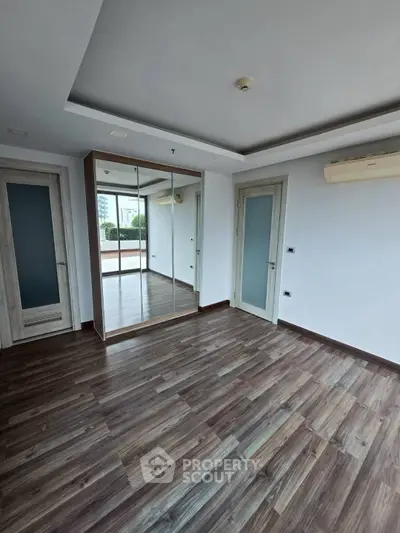 Spacious empty room with wooden flooring and mirrored closet doors.