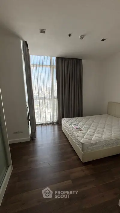 Spacious bedroom with large window and city view, featuring a comfortable mattress and elegant curtains.