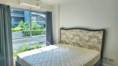 Bright bedroom with large window and elegant headboard, overlooking lush greenery.