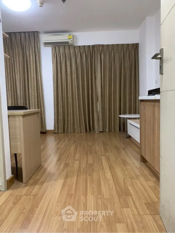 Spacious living room with wooden flooring and elegant curtains, featuring modern air conditioning.