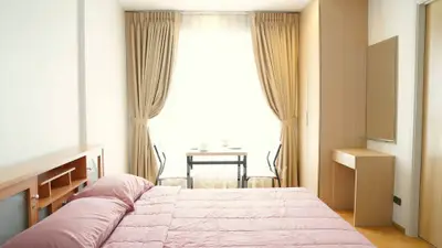Bright and cozy bedroom with large window and elegant curtains, featuring a comfortable bed and a small desk area.
