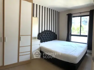 Modern bedroom with striped accent wall and large window offering natural light.