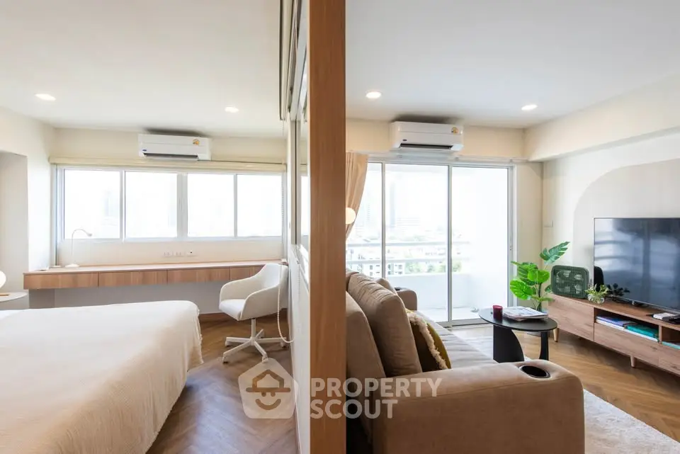Modern open-plan living room and bedroom with city view, stylish furniture, and natural light.