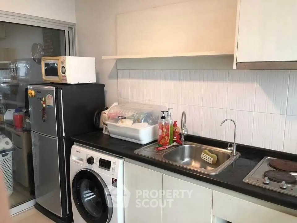 Modern kitchen with washing machine and microwave, sleek countertops, and ample storage space.