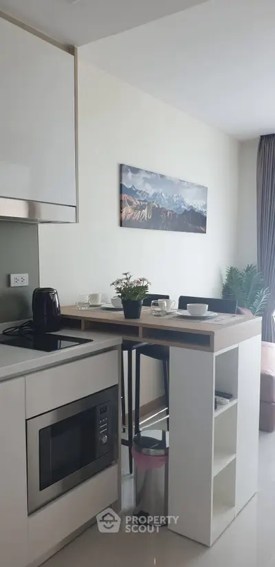Modern kitchen with sleek design, featuring a microwave, kettle, and stylish breakfast bar with mountain view artwork.
