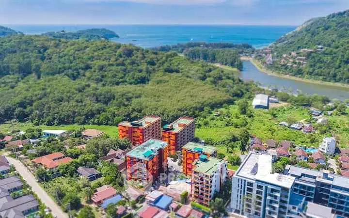 Aerial view of colorful apartment buildings surrounded by lush greenery and scenic ocean backdrop.