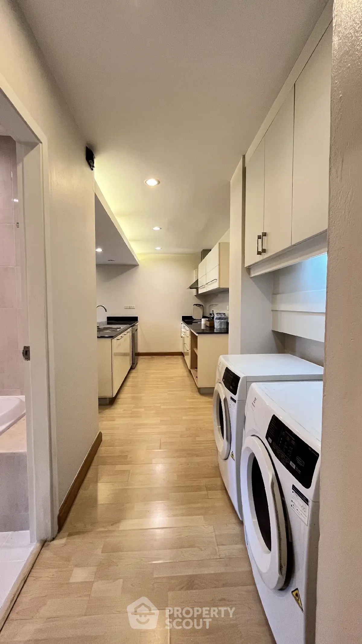 Spacious kitchen with modern appliances and laundry area, featuring sleek wooden flooring and ample storage.