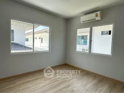 Bright and airy bedroom with large windows and modern air conditioning unit, offering a serene view of neighboring rooftops.