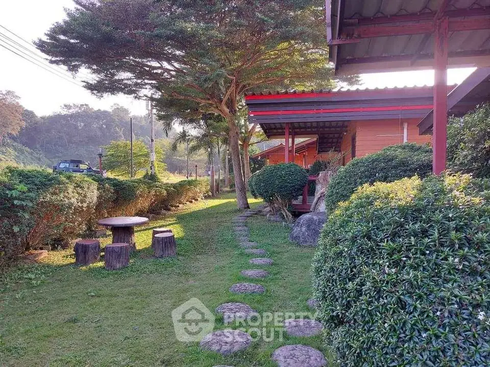 Charming garden pathway leading to rustic wooden cabins surrounded by lush greenery and scenic views.