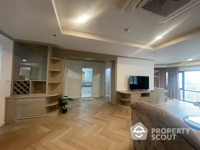 Spacious living room with elegant herringbone wood flooring, custom shelving, and ample natural light from large windows, perfect for entertaining and relaxation.