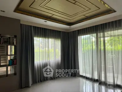 Spacious room with elegant ceiling design and large windows offering lush garden views.