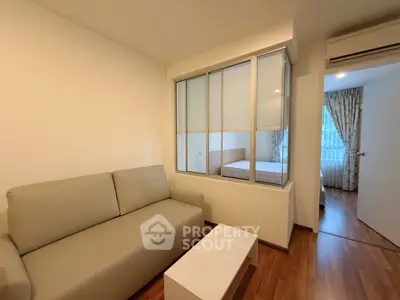 Cozy living room with beige sofa and view into bedroom through glass partition.