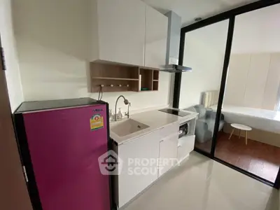 Modern compact kitchen with sleek white cabinetry and vibrant pink fridge in stylish apartment.