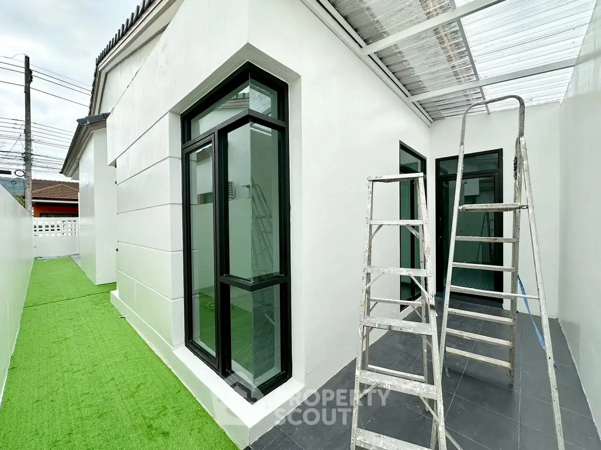 Modern exterior with large windows and artificial grass, featuring a ladder for maintenance.
