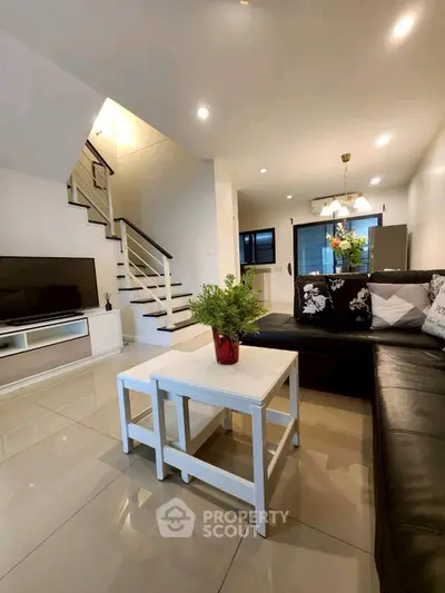 Modern living room with sleek design, black leather sofa, and elegant staircase in a stylish home.