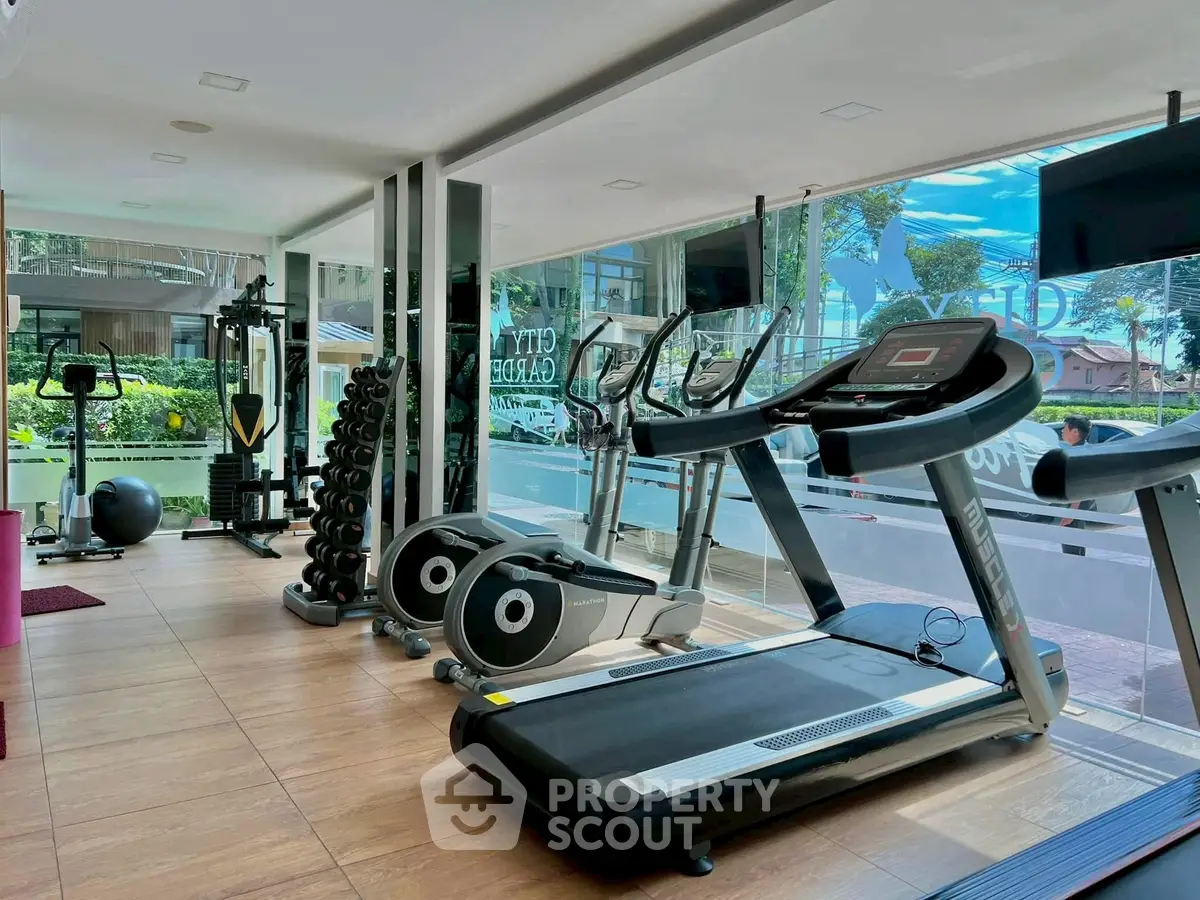 Modern gym with treadmills and weights in a bright, glass-walled space overlooking greenery.