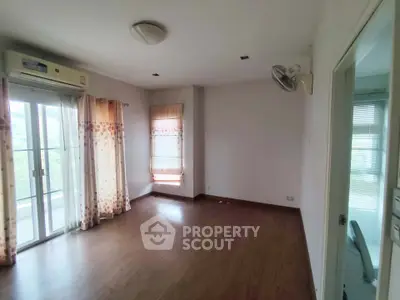 Spacious empty room with wooden flooring and large windows in a modern apartment.