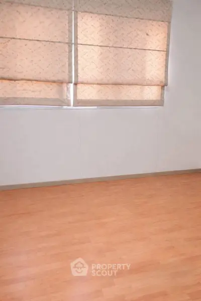 Spacious room with wooden flooring and large windows with blinds, perfect for customization.