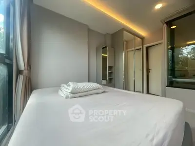 Modern bedroom with large window and mirrored closet doors, offering a bright and spacious feel.