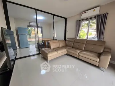 Modern living room with leather sofa and glass partition leading to dining area with fridge.