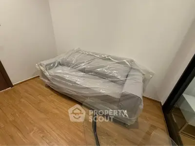 Modern living room with a new sofa wrapped in plastic on elegant wooden flooring.