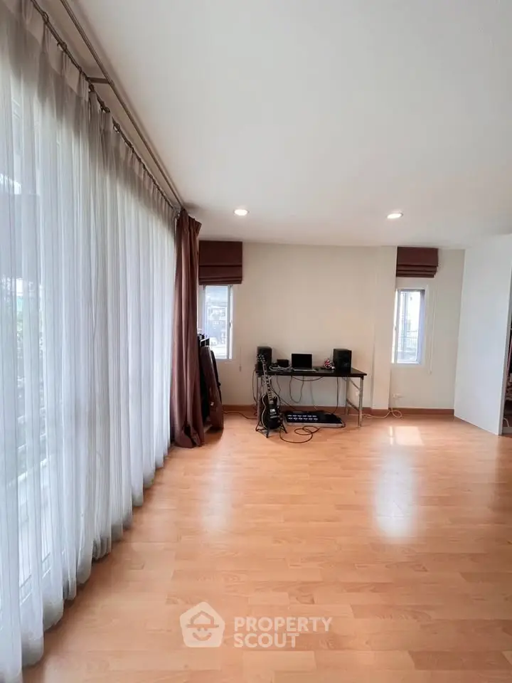 Spacious living room with wooden flooring and natural light, ideal for music enthusiasts.