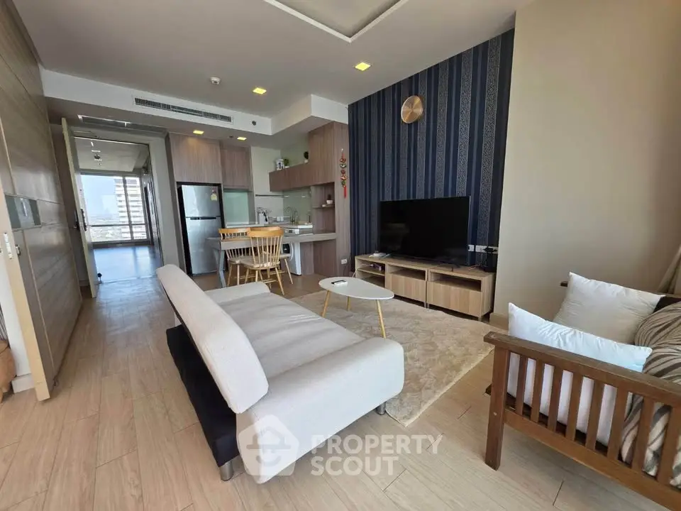 Modern living room with open kitchen, stylish decor, and natural light in a high-rise apartment.