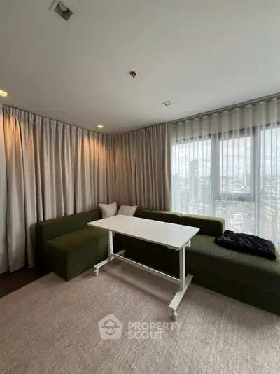 Modern living room with green sectional sofa and large windows offering city views.