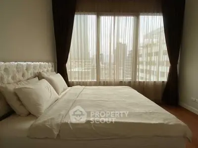 Cozy bedroom with large window offering city view, featuring elegant curtains and plush bedding.