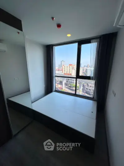 Modern bedroom with large window offering city view in high-rise apartment.