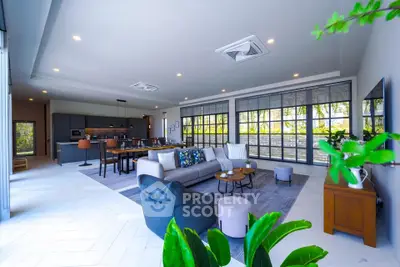 Spacious modern living room with open kitchen and large windows offering garden views.