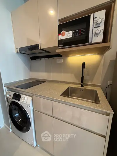Modern compact kitchen with washing machine and microwave, sleek cabinetry and efficient layout.