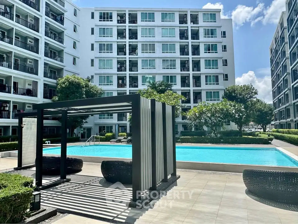 Modern apartment complex with pool and outdoor seating area under clear blue sky.