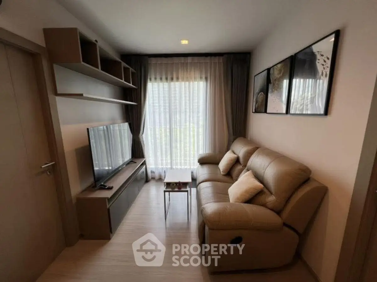 Cozy living room with modern sofa, TV, and natural light through large window.