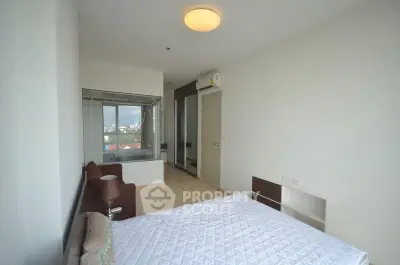 Spacious bedroom with large window and modern decor in a high-rise apartment.