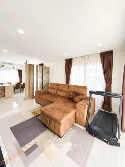 Spacious living room with modern decor and treadmill, featuring a large brown sofa and ample natural light.