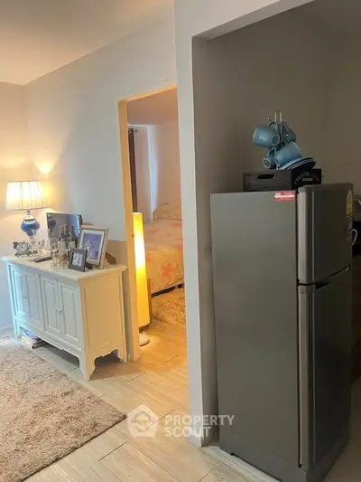 Cozy living area with modern fridge and elegant decor, leading to a charming bedroom.