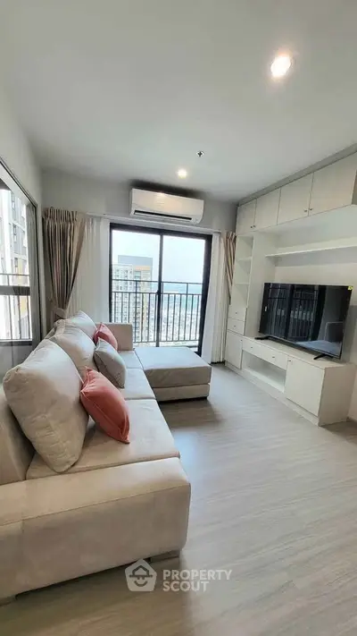 Modern living room with large windows and city view, featuring a cozy sectional sofa and built-in entertainment unit.