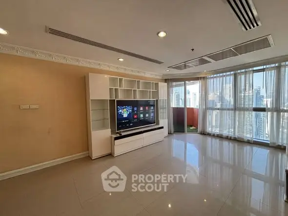Spacious living room with modern entertainment center and city view balcony.