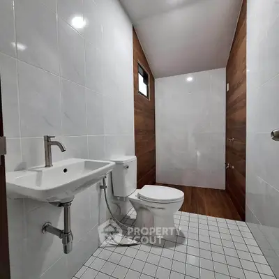Modern bathroom with sleek white tiles and wooden accents, featuring a contemporary sink and toilet.