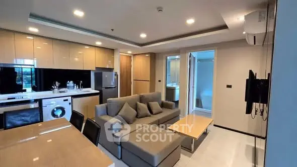 Modern open-layout living room with kitchen, featuring a washing machine and sleek furniture.