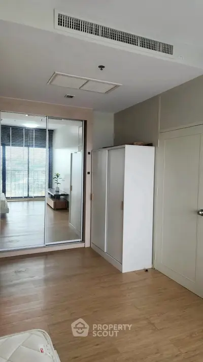 Modern bedroom with mirrored wardrobe and wooden flooring, offering a sleek and spacious design.