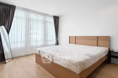 Spacious bedroom with large window and modern furnishings in a bright apartment.